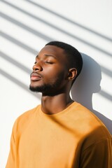 A man in a yellow shirt is sitting in the shade. He is looking away from the camera and he is in a relaxed state