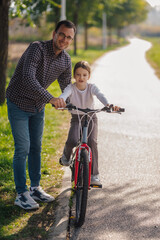 Obraz premium Father teaching daughter how to ride bicycle in park