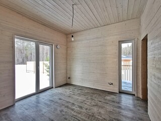 Bright, empty interior of a wooden house with large windows and snowy landscape outside during winter