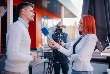 Journalist interviewing businessman for television news story outdoors