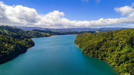 Obraz premium Aerial view of a serene river flowing through lush green hills under a bright blue sky with fluffy white clouds; ideal for travel brochures