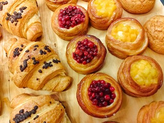 Freshly baked pastries with fruit fillings and chocolate croissants displayed on a wooden board in a bakery