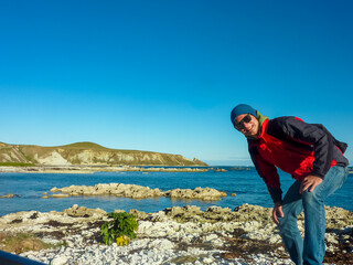 Tourist man discovers rugged, rocky coastline meets calm waters of Pacific ocean along Kaikoura Coast Track, Canterbury, New Zealand. Majestic mountain range visible. Serene seascapes. Coastal scenery