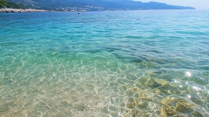 Obraz premium Crystal-clear coastal water, sunny beach, hills background; ideal for travel brochures