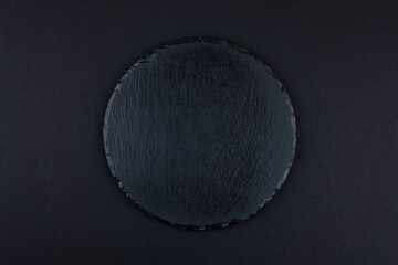 Round rustic black slate stone plate, on dark background