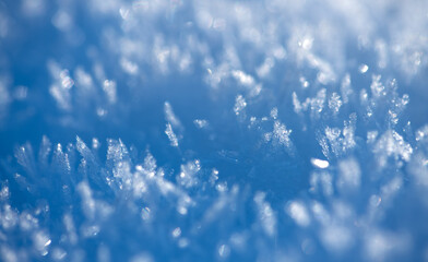 Obraz premium Macro shot of tiny ice crystals in sunlight with selective focus. Blue shimmering deep frozen snow. Winter background in blue tones with glittering light reflections. Structures of crystalline water.