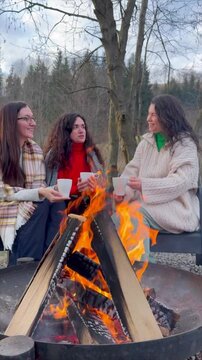 Friends enjoying warm drinks around a cozy outdoor fire in nature