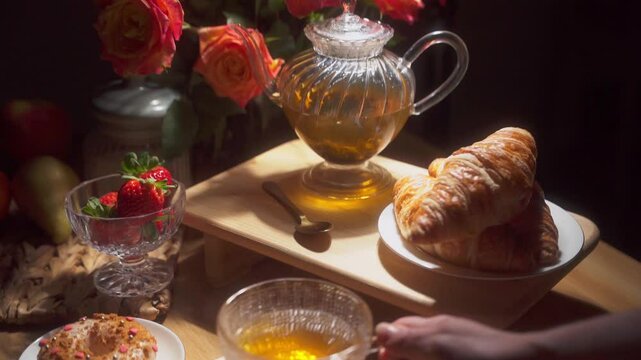 Hand Reaching for a Tea Cup and a Croissant. Romantic setup with Roses