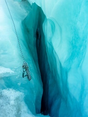 Deep crevasse in Franz Josef Glacier, Westland Tai Poutini National Park, South Island New Zealand. Climbing rope disappears in icy depths. Glimpse into stunning, perilous, beauty of frozen landscape