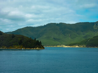 Untamed beauty of sea-drowned valleys Marlborough Sounds seen from Cook Straitn New Zealand. Forested hills meet vast Pacific Ocean under dramatic cloudy sky. Ferry trip between Picton and Wellington