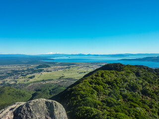 Panoramic view of Lake Taupo seen from top of Mt Tauhara, Waikato, North Island New Zealand. Surrounded by lush green hills covered with forest and snow-capped Kaimanawa mountain range. Tahurangi peak