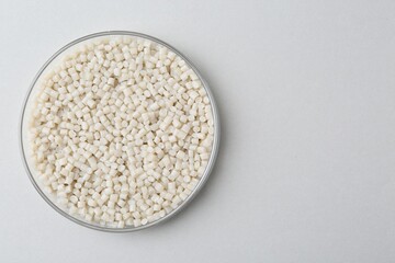 Plastic granules in petri dish on gray background, top view. Space for text