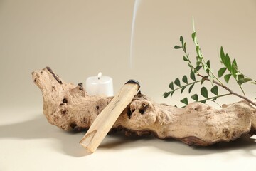 Smoldering palo santo stick, snag, green branch and burning candle on beige background