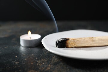 Smoldering palo santo stick and burning candle on dark table, closeup