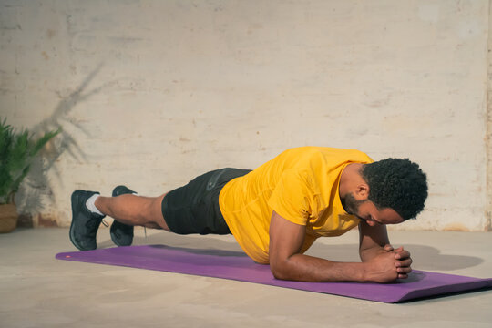 A dedicated man consistently performs a challenging plank exercise on a bright purple yoga mat in an indoor setting