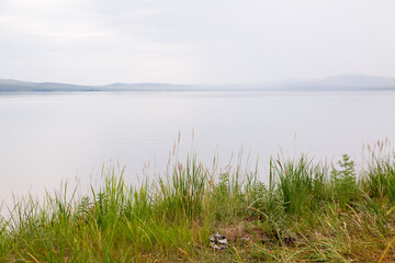 Natural background of lake water, sky and shore with grass in the foreground