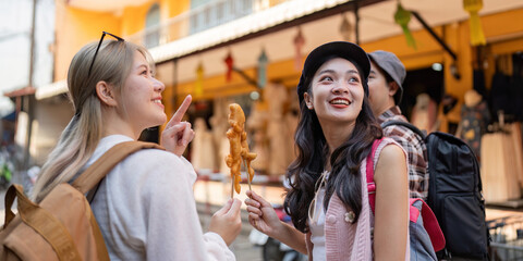 Friends sharing laughter while enjoying street food, exploring a vibrant market during their travel...