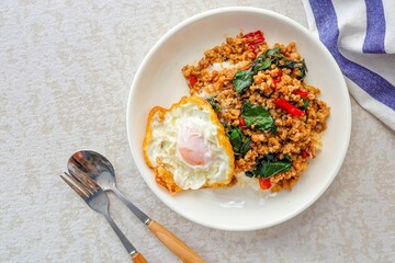 Homemade Rice topped with stir fried Thai basil with minced pork and fried egg in white plate, pad ka praow moo sap