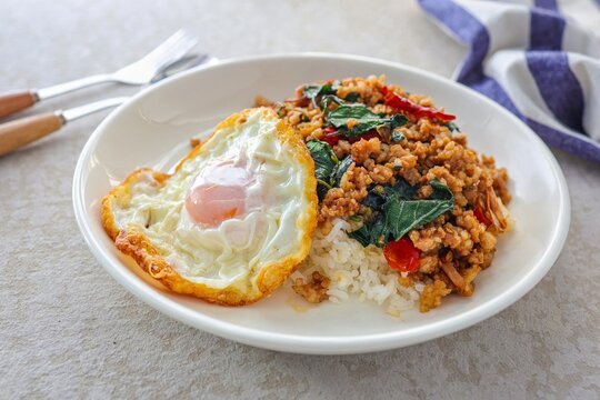 Homemade Rice topped with stir fried Thai basil with minced pork and fried egg in white plate, pad ka praow moo sap