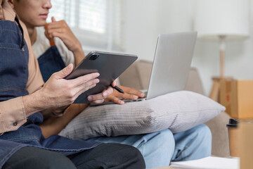 Fototapeta premium Couple reviewing plans on a tablet and laptop while seated comfortably in their modern living room