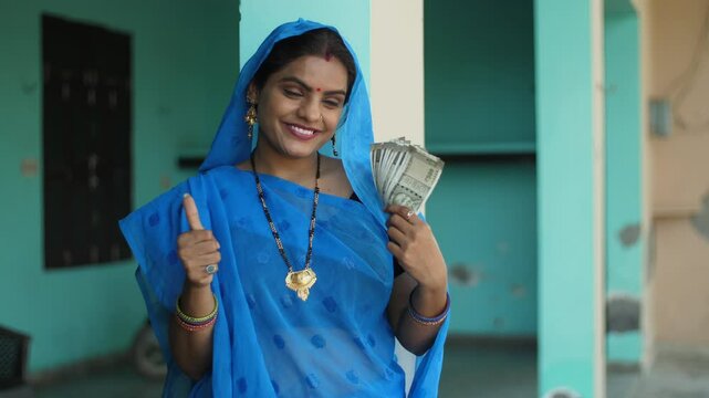 Happy Indian house wife proudly showing her last month's salary - working woman  financially independent villager. A portrait of a village woman holding 500 rupees notes from her saved earnings - h...