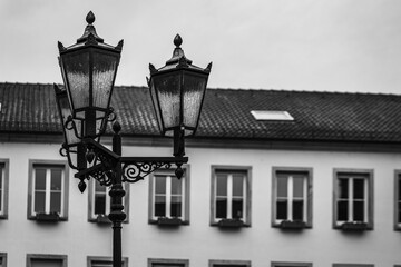 Old-fashioned street lamps illuminate a quaint building in a European town during a cloudy day