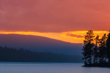 Fototapeta premium Beautiful sunset over Lake Burusjon in Sweden with vibrant colors reflecting off the water and silhouetted trees lining the shore