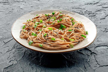 Soba, Japanese buckwheat noodles, boiled, on a plate on a black slate background
