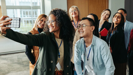 Diverse group of successful coworkers taking a joyful selfie at work during a daytime event in a modern office setting