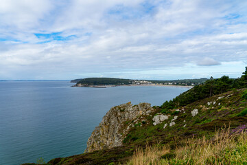 Fototapeta premium Vue panoramique sur la baie de Morgat et la mer d’Iroise depuis les falaises, sous un ciel bleu parsemé de nuages.