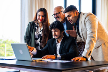Group of Indian professionals in formal attire working with documents and laptop, discussing ideas