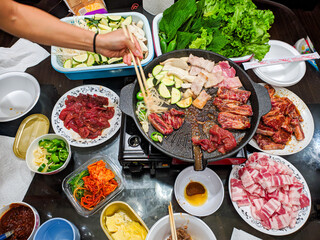 Korean BBQ (Gogi-gui) with various meats, vegetables, and side dishes. Interactive dining experience, social gathering. Ideal for Korean food blogs, restaurant promotions, and culinary publications.
