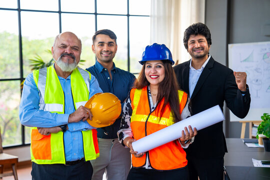 Indian Asian Engineers and architects in fluorescent jackets, hard hats smiling confidently indoors
