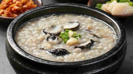 A bowl of comforting Korean congee juk with abalone, served with a side of kimchi and pickled radish.