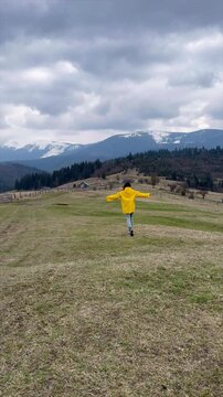 Girl in a yellow raincoat joyfully running in a beautiful mountainous landscape