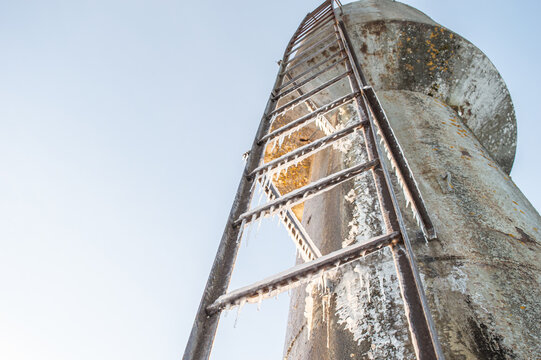 an ice staircase leading up to a metal water tower. The old metal staircase is covered with icicles from bottom to top. a water tower against the sky. High quality photo