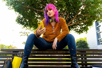 Body positive autistic girl with pink and purple hair using smartphone on bench