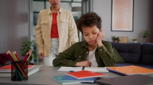 African American family at home tired sad little child kid boy studying education writing difficult homework problem son crying upset woman girl female mother coming room tickling talking support fun