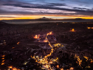 Aerial drone view of Göreme with lights on at dusk during sunrise, with hot air balloons preparing...
