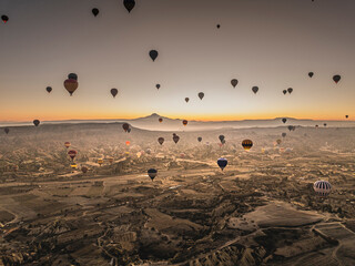 Aerial drone view of flying hot air balloons above the Rose Valley during sunrise with a clear sky in Cappadocia, and Mount Erciyes on the horizon