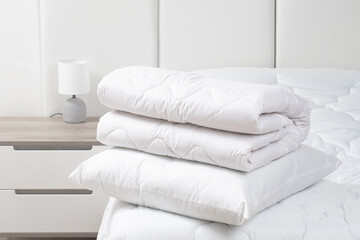 A bed with white pillows and a blanket, next to a bedside table with a lamp, daylight