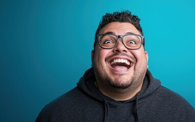 Fototapeta premium A happy plus-sized man with expressive laughter lines and glasses, wearing a dark gray hoodie, standing on a gradient blue backdrop