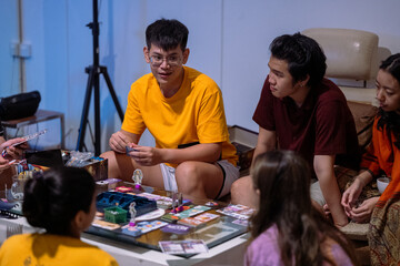 A group of Asian friends playing a board game in a cozy indoor setting. One participant in a yellow...