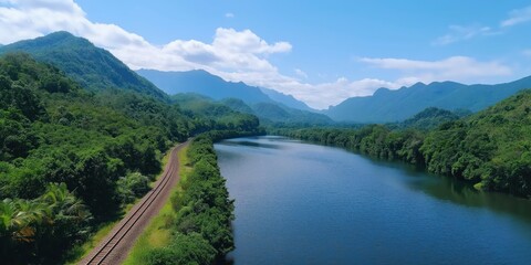 Fototapeta premium A sweeping view of a serene river winding through a dense evergreen forest, with a railway track curving along the edge of the trees