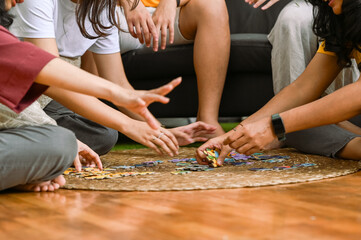 A group of Asian friends gathers indoors, enthusiastically collaborating on a puzzle game. They sit...