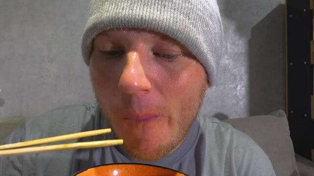 A young man eats pasta noodles with wooden chopsticks. Have dinner at home. Slow Motion.