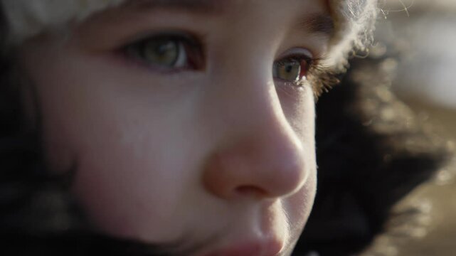 Portrait of a little girl looking away while standing outside on a cold day. A thinking child opens his eyes and looks into the distance outdoors. Face Eyes Serious Contemplative Child