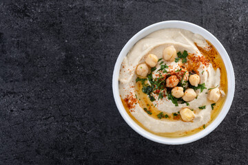 Chickpea hummus with olive oil, parsley and paprika in bowl on black background. Top view. Copy space