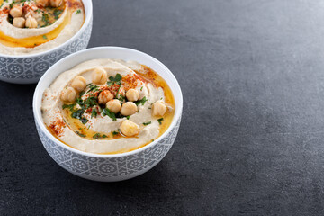 Chickpea hummus with olive oil, parsley and paprika in bowl on black background. Copy space