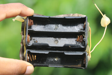 Old and rusty battery holder held in the hand on a natural background